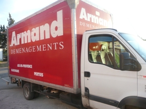 Camion de déménagement rouge “Armand Déménagements” prêt à partir, vue latérale et cabine blanche. Inclut le texte publicitaire sur le véhicule.